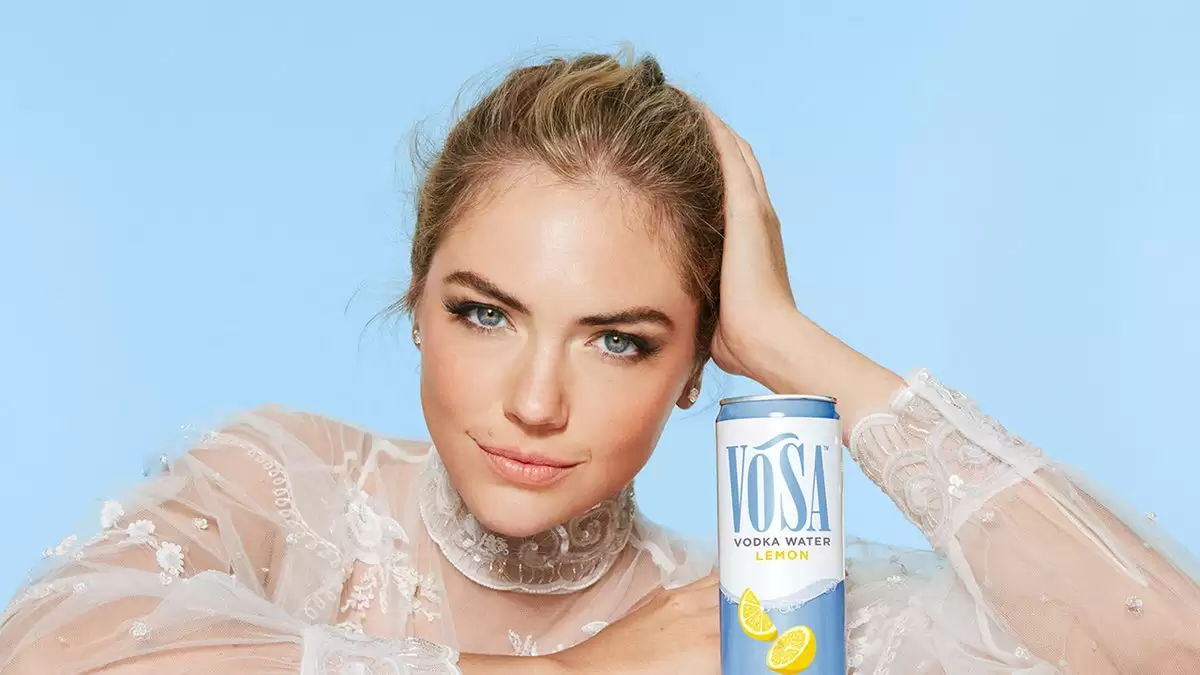 Kate Upton trong Chiếc váy ren cổ cao màu trắng tạo kiểu dáng bên cạnh một lon rượu Vosa Spirits